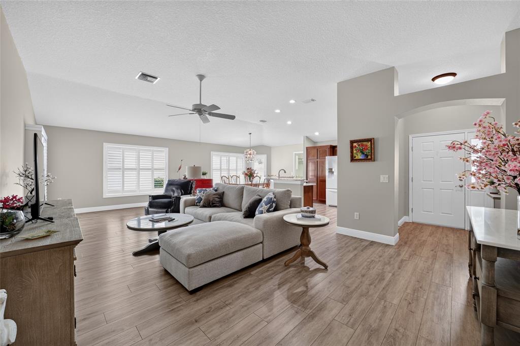 A living room with light wood flooring, a gray sectional sofa, and an open floor plan — 2408 SAFFRON LANE, THE VILLAGES, FL