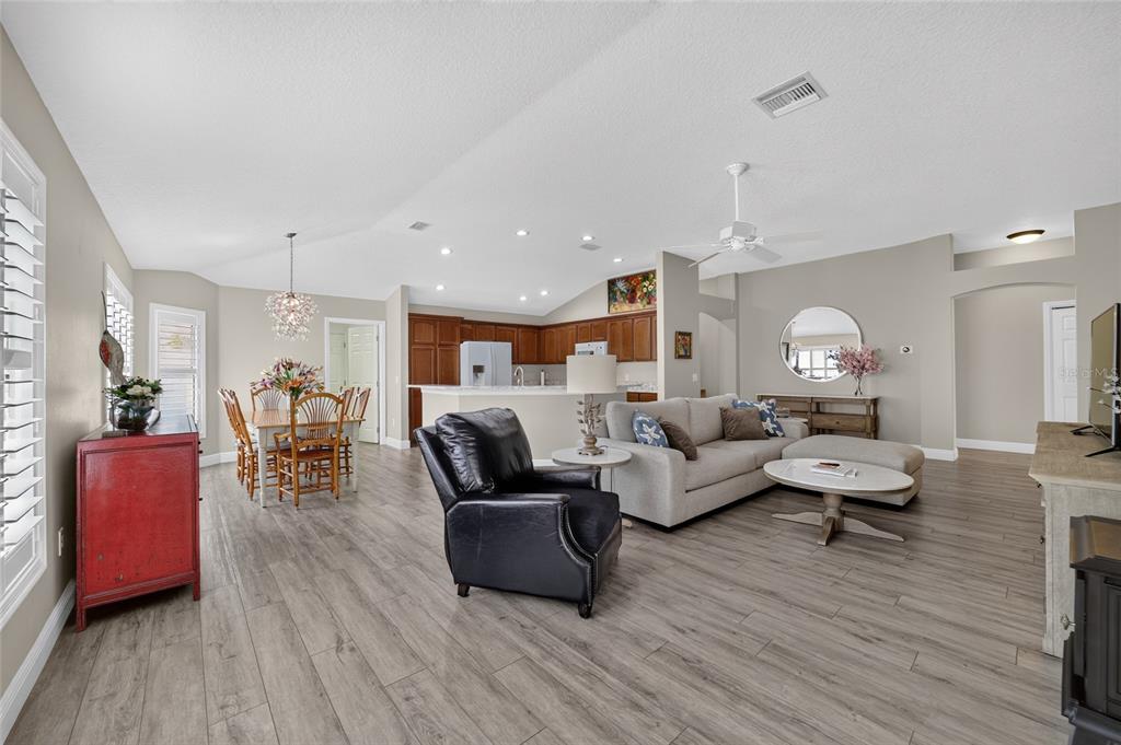 An open-concept living and dining area features wood-look tile flooring and a neutral color palette — 2408 SAFFRON LANE, THE VILLAGES, FL