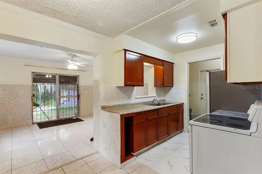 A kitchen with dark wood cabinets, marble-look flooring, and an adjacent room with sliding doors — 1227 MERRITT STREET, ALTAMONTE SPRINGS, FL