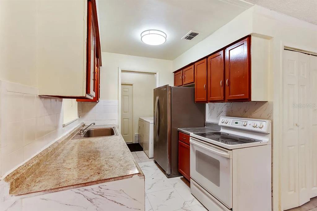 A kitchen features wood cabinets, granite countertops, stainless steel appliances, and white marble-patterned flooring — 1227 MERRITT STREET, ALTAMONTE SPRINGS, FL