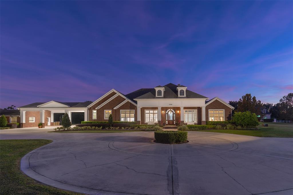 A large brick house with a circular driveway at dusk — 2780 VICKIE COURT, KISSIMMEE, FL