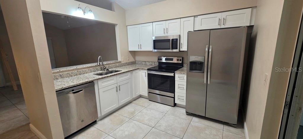 A kitchen features white cabinets, granite countertops, stainless steel appliances, and tile flooring — 10350 RIVA RIDGE TRAIL, ORLANDO, FL