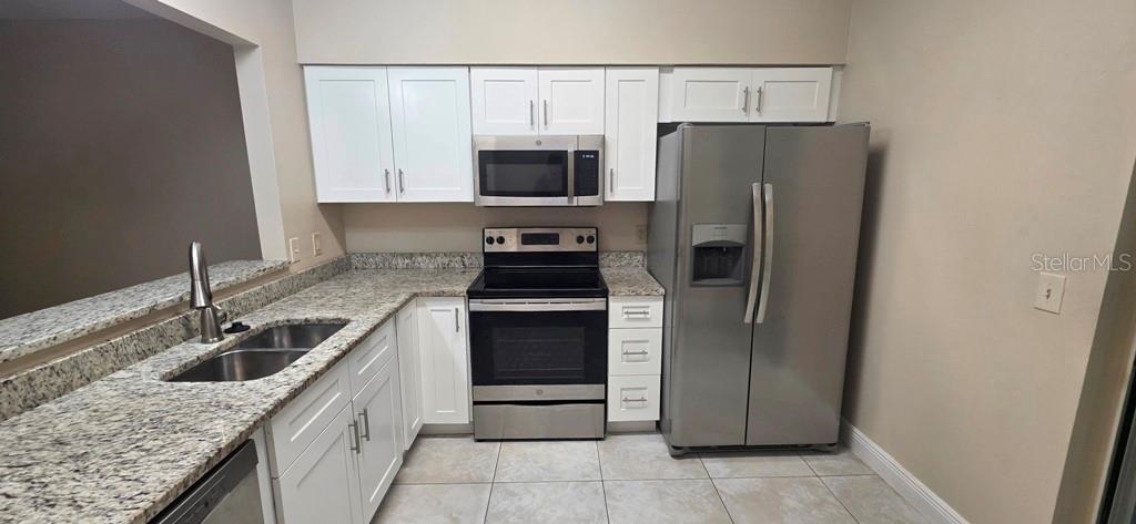 A kitchen features white cabinets, granite countertops, stainless steel appliances, and tile flooring — 10350 RIVA RIDGE TRAIL, ORLANDO, FL