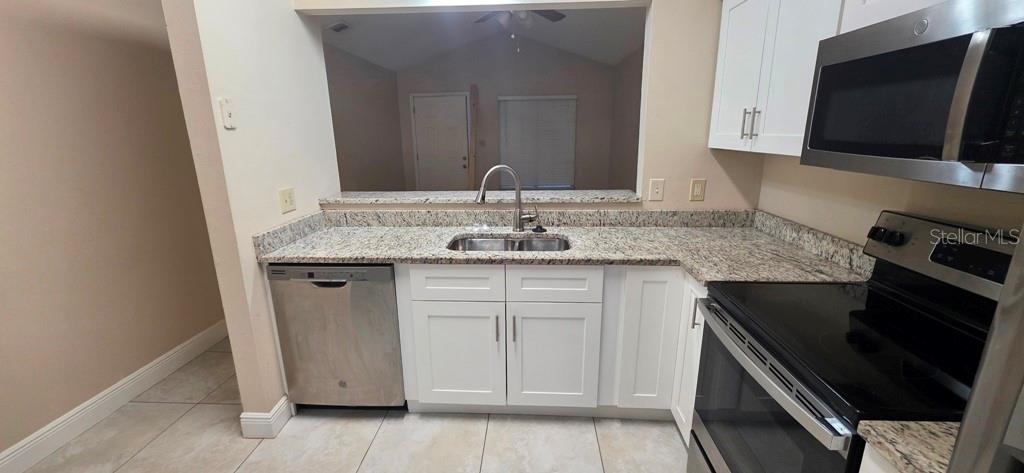 A kitchen features white cabinets, granite countertops, stainless steel appliances, and a pass-through window — 10350 RIVA RIDGE TRAIL, ORLANDO, FL