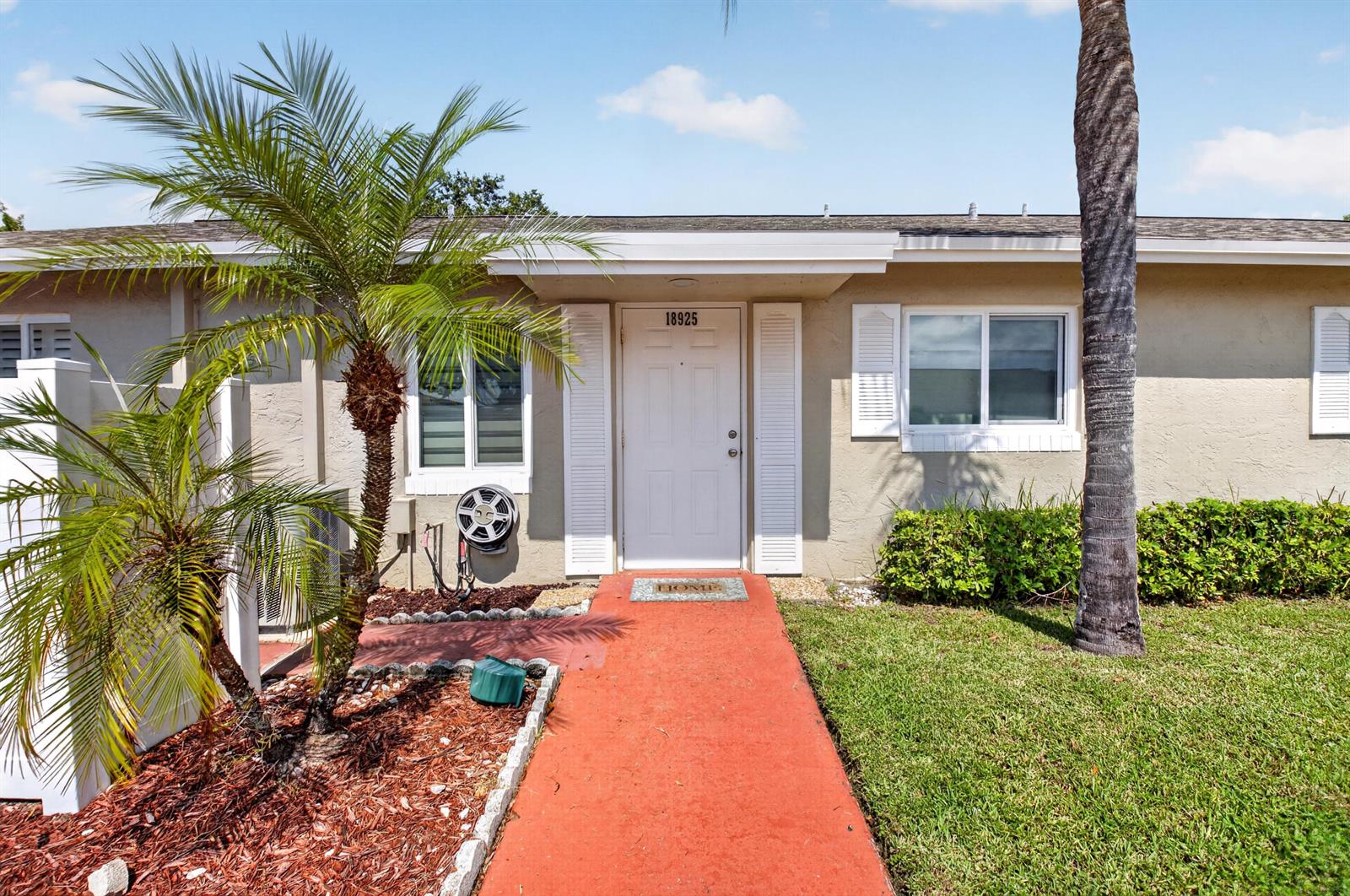A tan exterior home features a white front door, a red walkway, and palm trees — 18925 Argosy Drive # B, Boca Raton FL 33496, BOCA RATON, FL