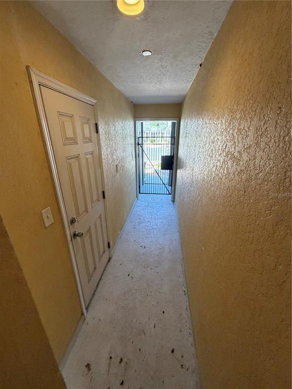 A narrow hallway with textured yellow walls leads to a metal gate at the end — 4817 TUSCAN LOON DRIVE, TAMPA, FL