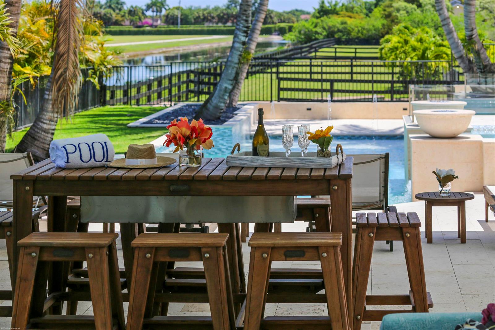 A wooden bar table with stools sits on a patio overlooking a swimming pool — 14991 Palm Beach Point Boulevard, Wellington FL 33414, WELLINGTON, FL