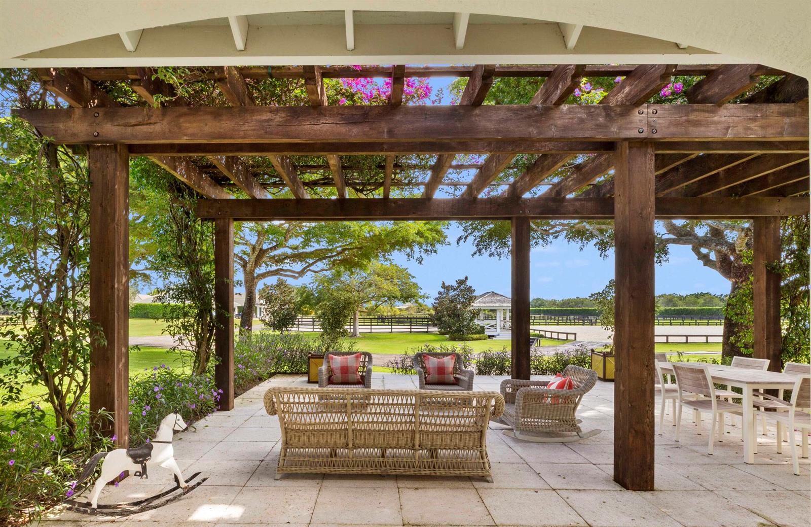 A covered outdoor patio features wicker furniture, a rocking horse, and a wooden pergola — 14991 Palm Beach Point Boulevard, Wellington FL 33414, WELLINGTON, FL