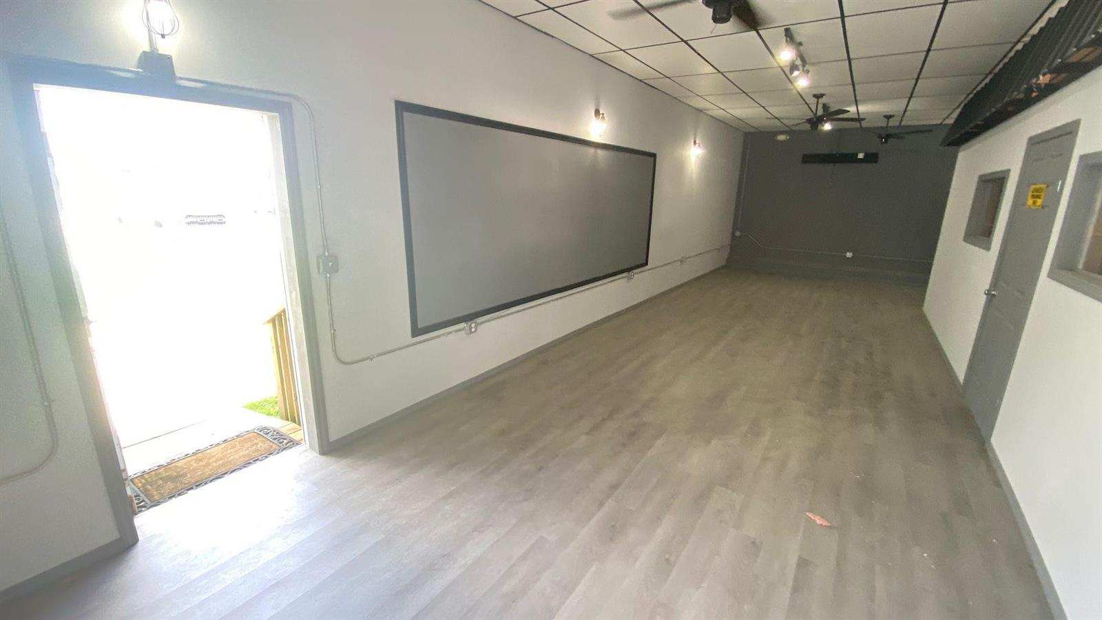 An empty room with light wood-look flooring, a large wall-mounted screen, and a doorway — 4650 US Highway 27, Sebring FL 33870, SEBRING, FL