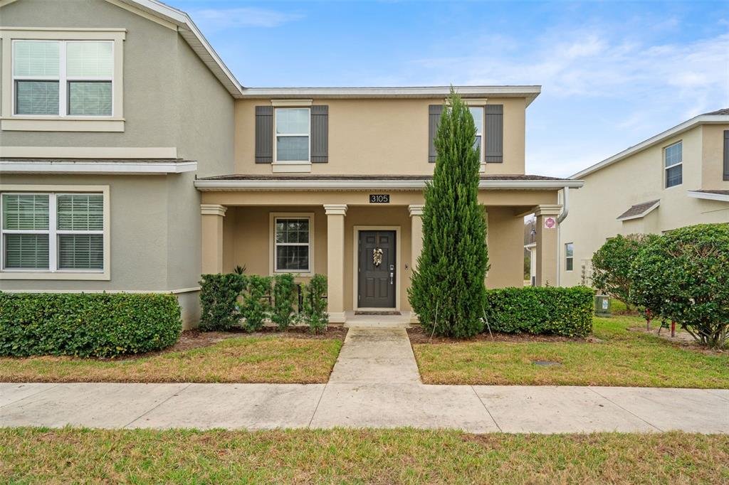 The exterior of a two-story tan house features a covered front porch and landscaping — 3105 AQUA VIRGO LOOP, ORLANDO, FL