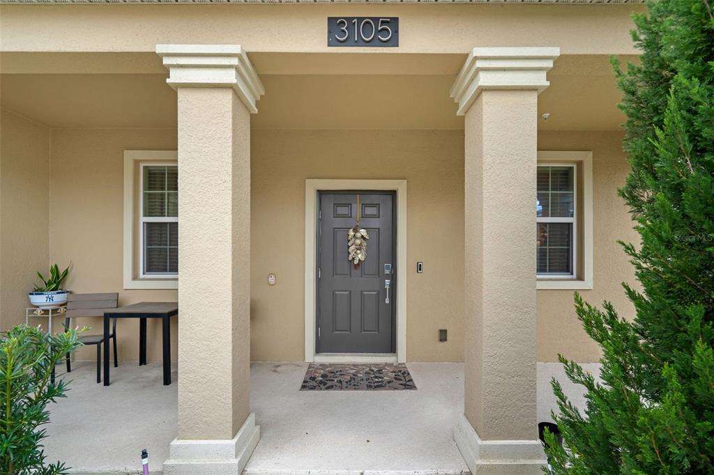 A covered front porch features two beige columns, a gray front door, and a small table — 3105 AQUA VIRGO LOOP, ORLANDO, FL