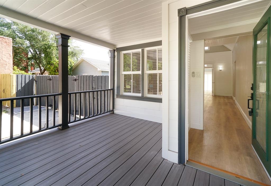 A covered wooden porch with black railings leads into a home with light wood flooring — 437 N SHINE AVENUE, ORLANDO, FL