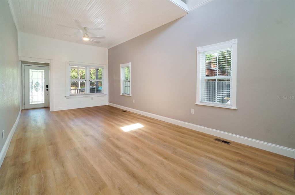 An empty living room features light wood flooring, white beadboard ceilings, and three windows — 437 N SHINE AVENUE, ORLANDO, FL