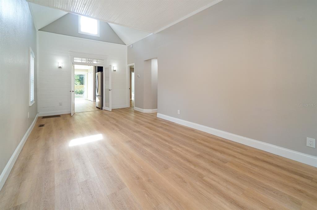 An empty room with light wood-look flooring, vaulted ceilings, and a doorway leading to a kitchen — 437 N SHINE AVENUE, ORLANDO, FL