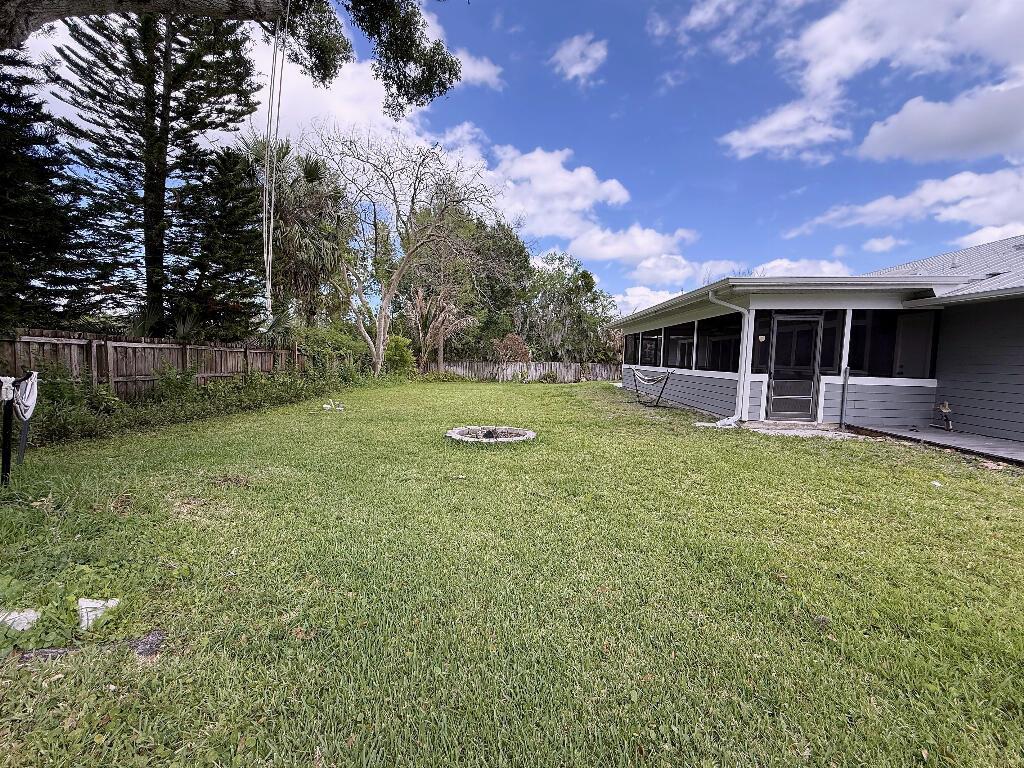 A grassy backyard features a circular fire pit and a screened-in porch on the house — 2402 River Hammock Lane, Fort Pierce FL 34981, FORT PIERCE, FL