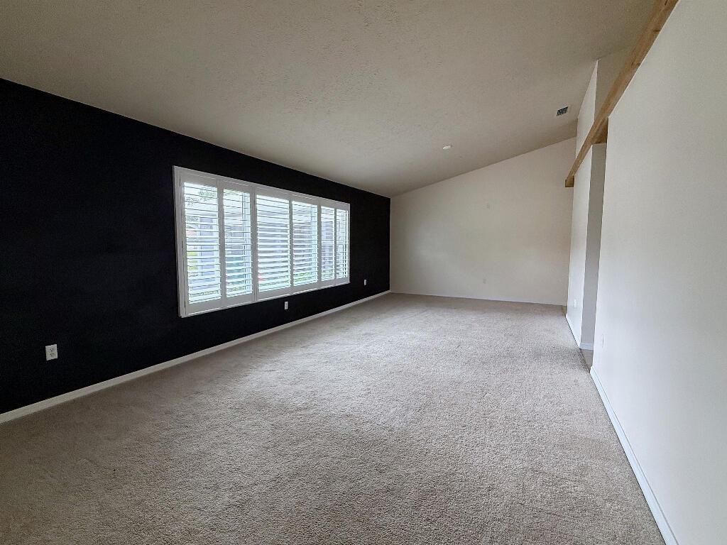 An empty living room features a dark accent wall, plantation shutters, and beige carpeting — 2402 River Hammock Lane, Fort Pierce FL 34981, FORT PIERCE, FL