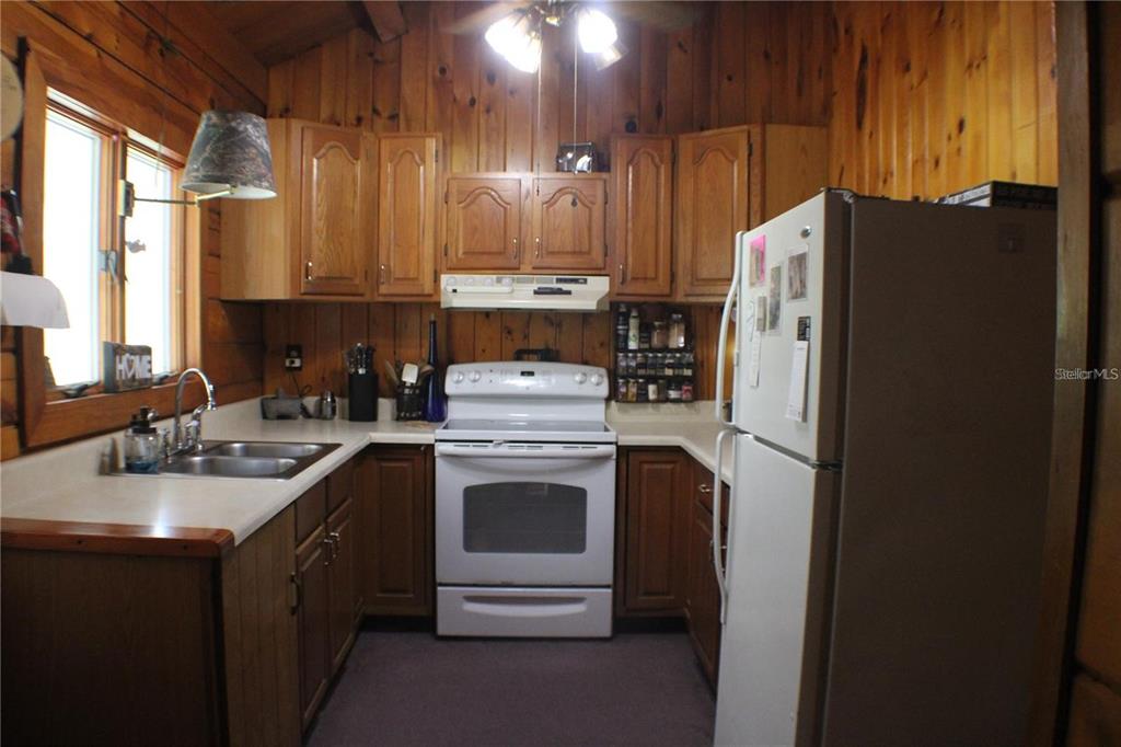 A kitchen features wood-paneled walls, oak cabinets, white appliances, and a double-basin sink — 3045 YORKSHIRE DRIVE, DELTONA, FL
