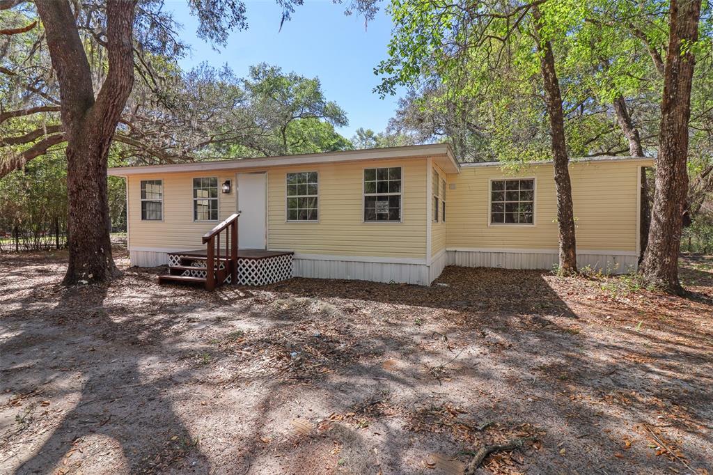 A yellow single-wide mobile home sits in a wooded lot with a small wooden porch — 6111 KLARE DRIVE, KEYSTONE HEIGHTS, FL