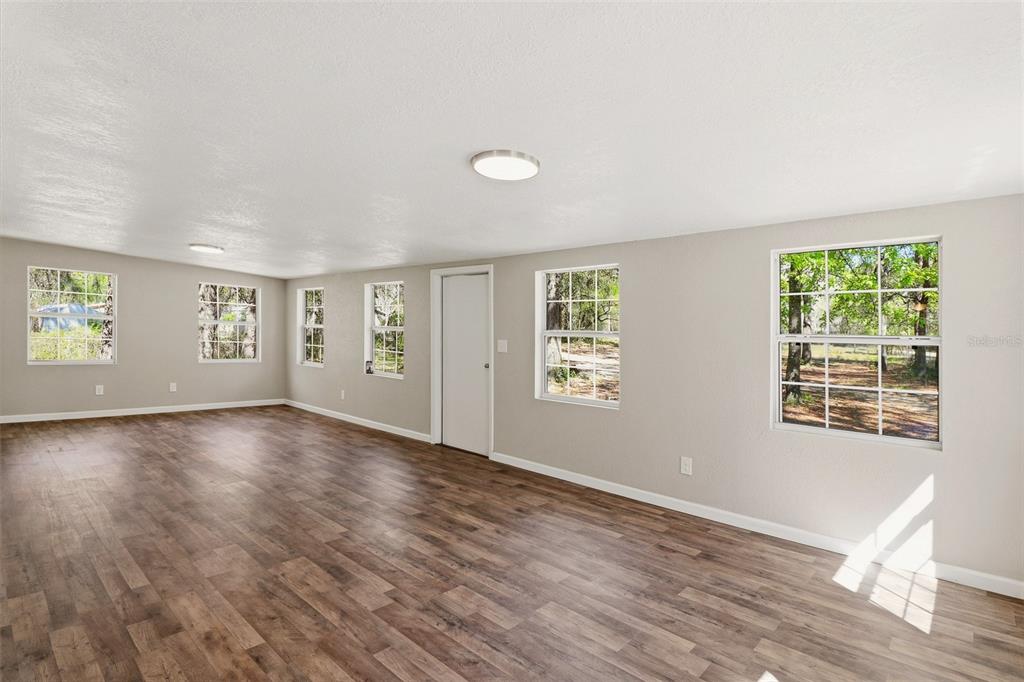 A spacious room with light gray walls, wood-look flooring, and multiple windows — 6111 KLARE DRIVE, KEYSTONE HEIGHTS, FL