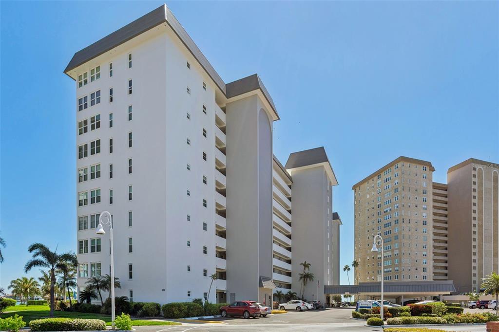 A multi-story white apartment building stands next to a parking lot under a clear sky — 5130 BRITTANY DRIVE S UNIT 1002, ST PETERSBURG, FL