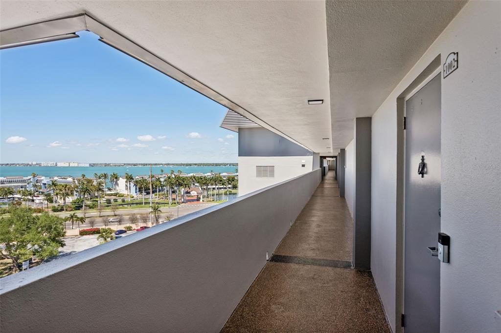 An outdoor apartment hallway features a gray door, textured flooring, and a view of water — 5130 BRITTANY DRIVE S UNIT 1002, ST PETERSBURG, FL