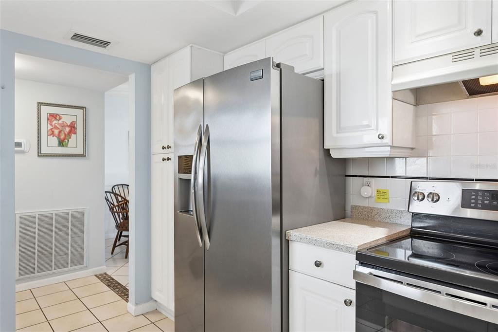 A kitchen features white cabinets, stainless steel appliances, and a tiled backsplash — 5130 BRITTANY DRIVE S UNIT 1002, ST PETERSBURG, FL