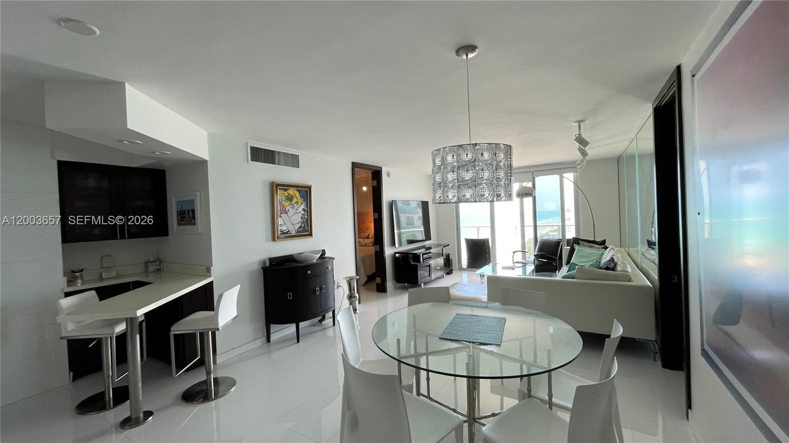 An open-plan living and dining area features white tile floors, a glass table, and kitchen — 5701 Collins Ave # 1714, Miami Beach FL 33140, MIAMI BEACH, FL