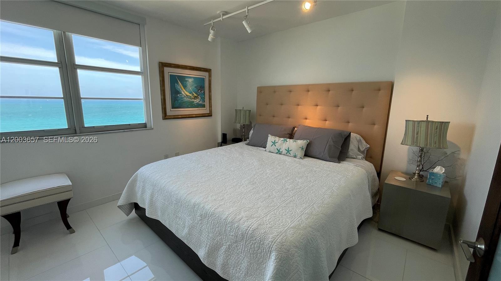A bedroom features a king bed, tufted headboard, and a large window overlooking the ocean — 5701 Collins Ave # 1714, Miami Beach FL 33140, MIAMI BEACH, FL