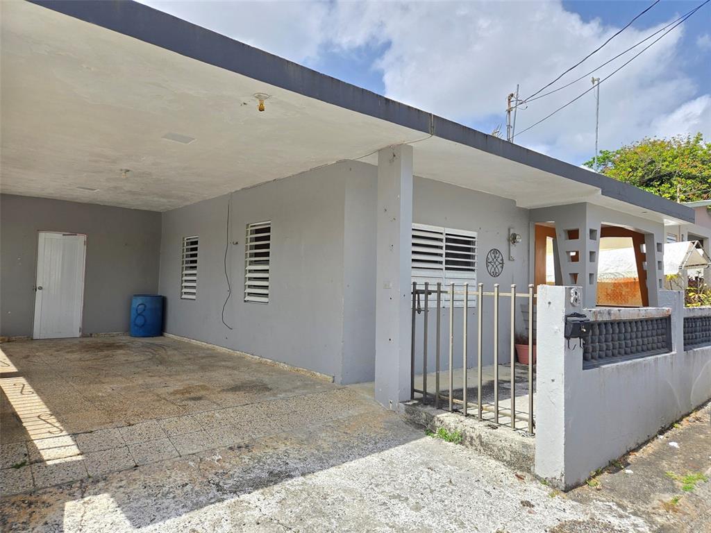 A gray house exterior features a covered carport, a gated entrance, and louvered windows — CALLE NAZARET SOLAR 403A COMUNIDAD SAN LUIS, AIBONITO, PR