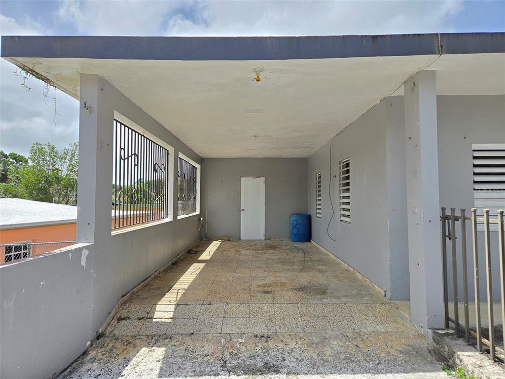 A covered concrete carport features tiled flooring, gray walls, and a white entry door — CALLE NAZARET SOLAR 403A COMUNIDAD SAN LUIS, AIBONITO, PR