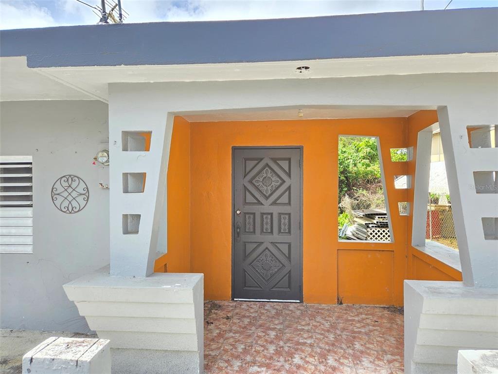 The exterior of a house features a covered porch with an orange wall and decorative blocks — CALLE NAZARET SOLAR 403A COMUNIDAD SAN LUIS, AIBONITO, PR