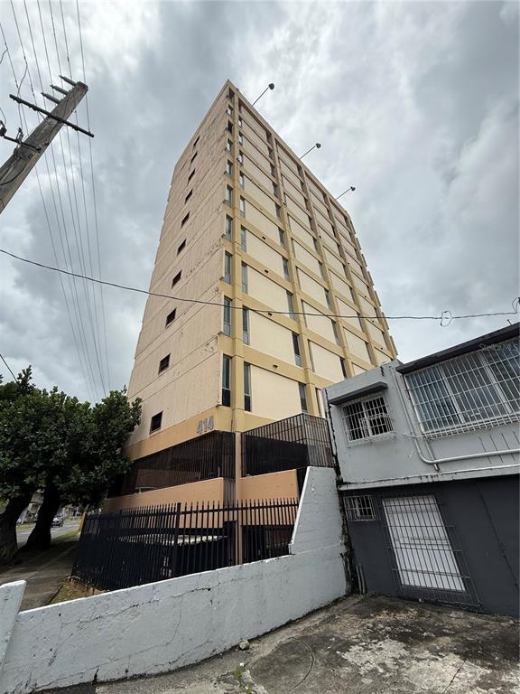 A tall, multi-story apartment building stands behind a black metal fence and a concrete wall — 414 MUÑOZ RIVERA AVENUE UNIT 6A & 6B, SAN JUAN, PR