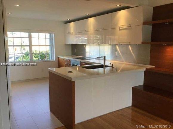 A modern kitchen features white glossy cabinets, a stainless steel backsplash, and a wooden island — 14340 SW 57th Ln # 204, Miami FL 33183, MIAMI, FL