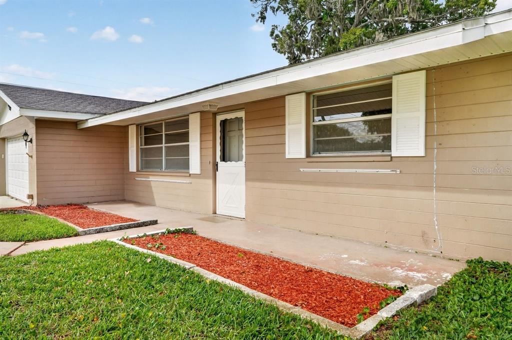 A tan house exterior features a concrete porch, white shutters, and red mulch landscaping — 2342 CITRUS AVENUE, SOUTH DAYTONA, FL