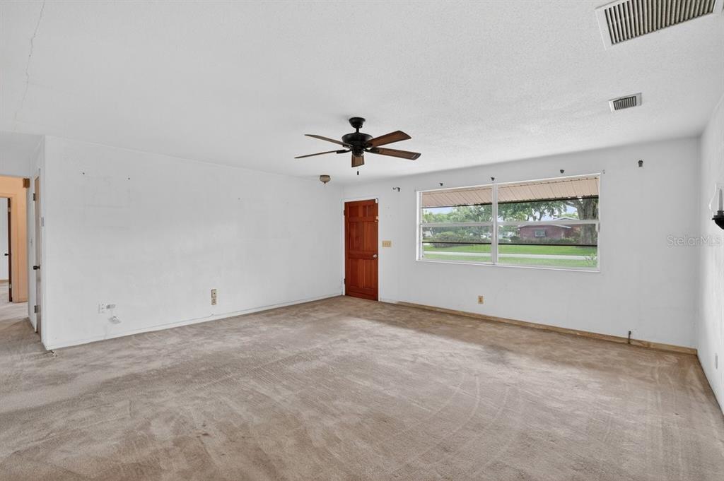 A carpeted living room features white walls, a ceiling fan, and a wooden exterior door — 2342 CITRUS AVENUE, SOUTH DAYTONA, FL