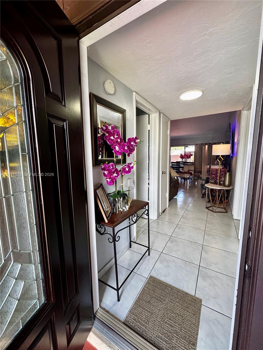 An entryway features a console table with orchids and a mirror, leading into a tiled hallway — 12316 SW 119th Ln, Miami FL 33186, MIAMI, FL