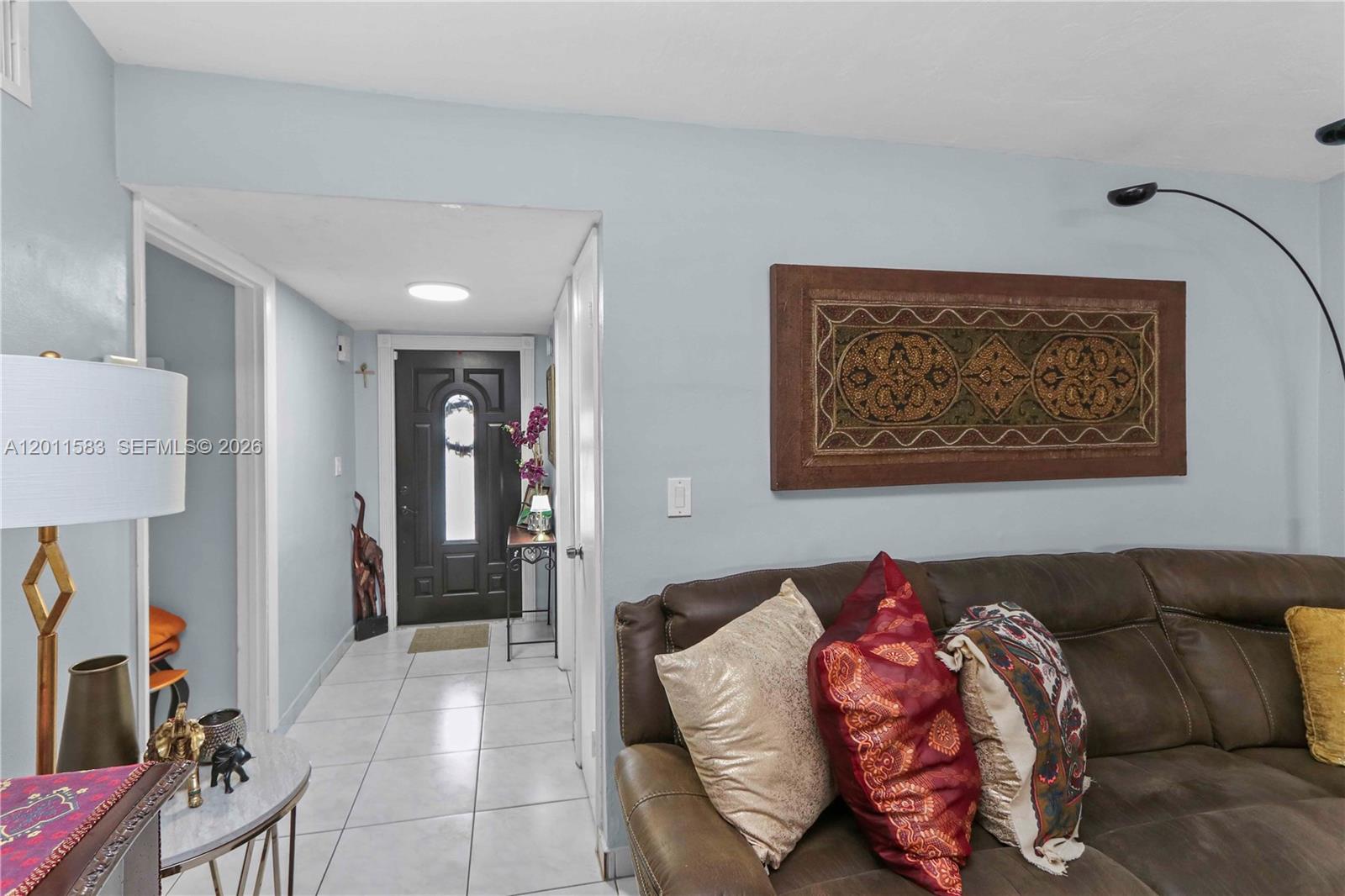 A living room with a brown leather sofa leads to a tiled entryway with a dark door — 12316 SW 119th Ln, Miami FL 33186, MIAMI, FL