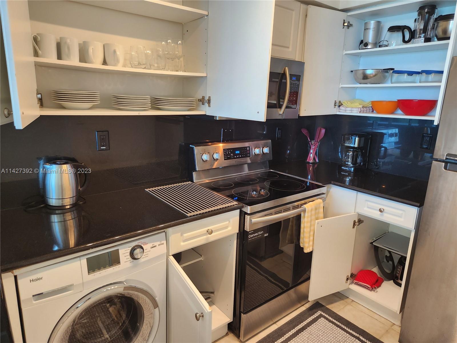 A kitchen features black countertops, stainless steel appliances, white cabinetry, and an integrated washing machine — 2501 S Ocean Dr # 512, Hollywood FL 33019, HOLLYWOOD, FL