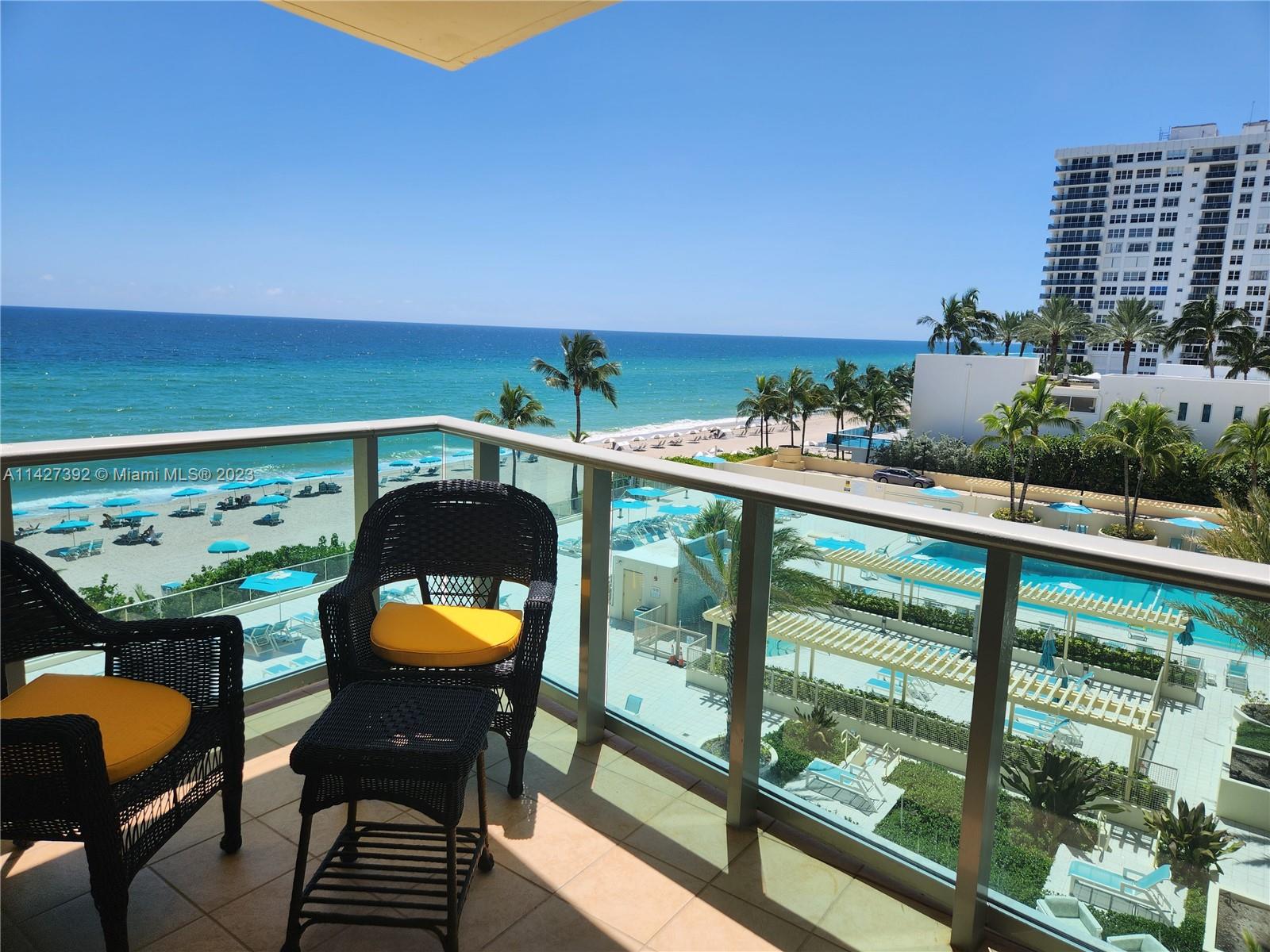 A balcony with wicker chairs overlooks a swimming pool, a sandy beach, and the ocean — 2501 S Ocean Dr # 512, Hollywood FL 33019, HOLLYWOOD, FL