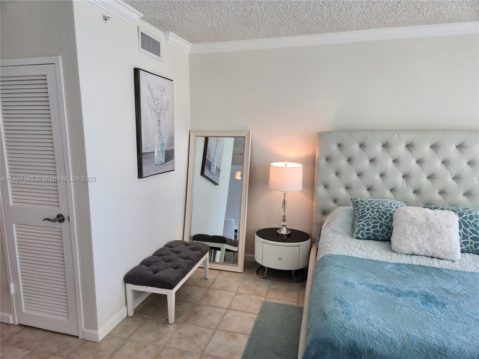 A bedroom features a tufted headboard, a floor mirror, a nightstand with a lamp, and bench — 2501 S Ocean Dr # 512, Hollywood FL 33019, HOLLYWOOD, FL