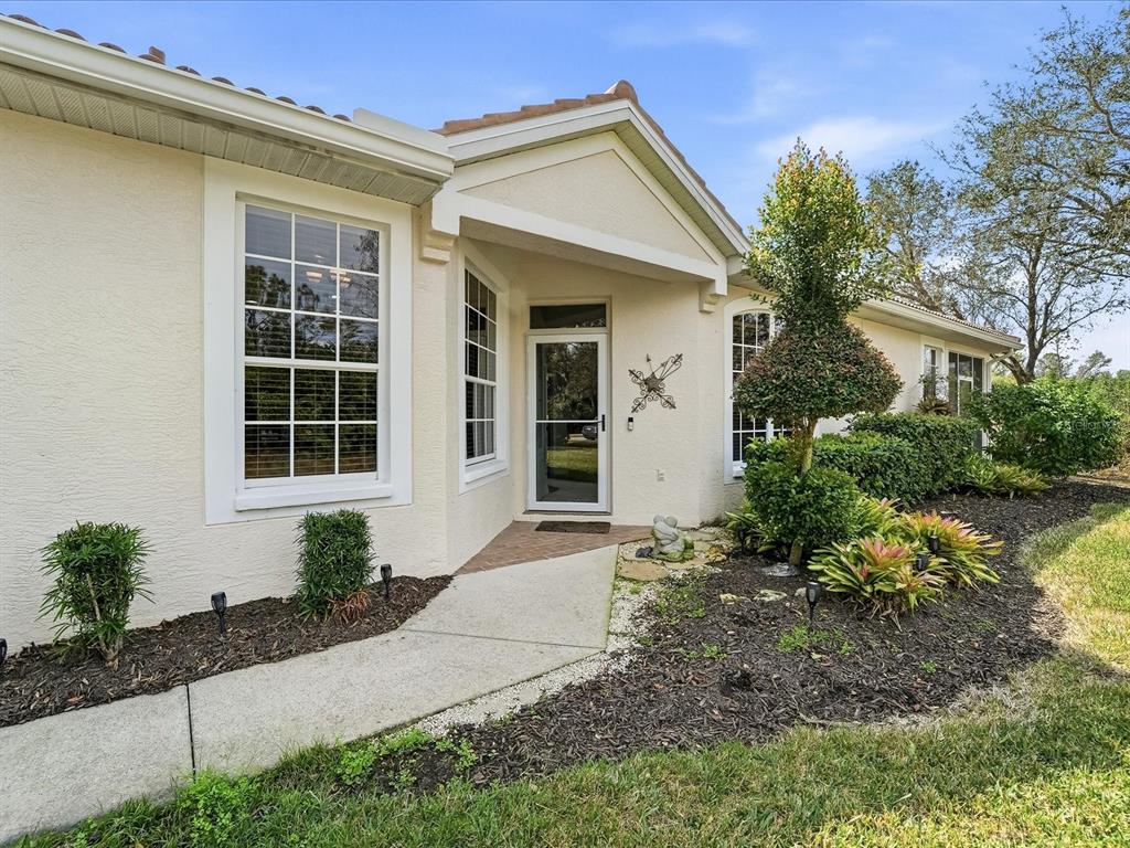 A beige stucco house exterior features a front entryway, a walkway, and landscaped garden beds — 4693 WHISPERING OAKS DRIVE, NORTH PORT, FL