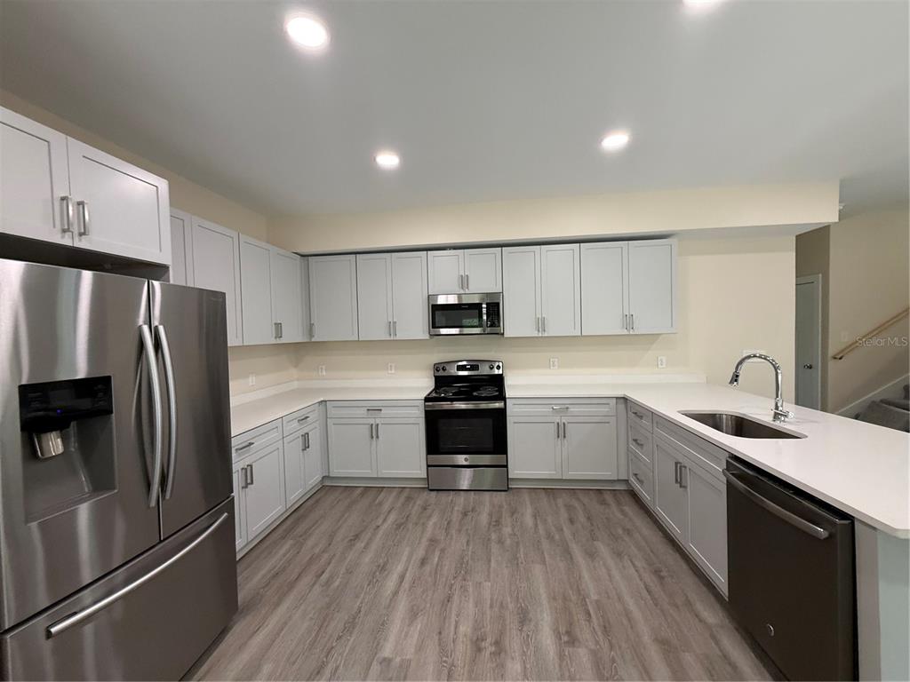 A modern kitchen features light gray cabinets, stainless steel appliances, and white countertops — 4409 NW 31ST AVENUE, GAINESVILLE, FL