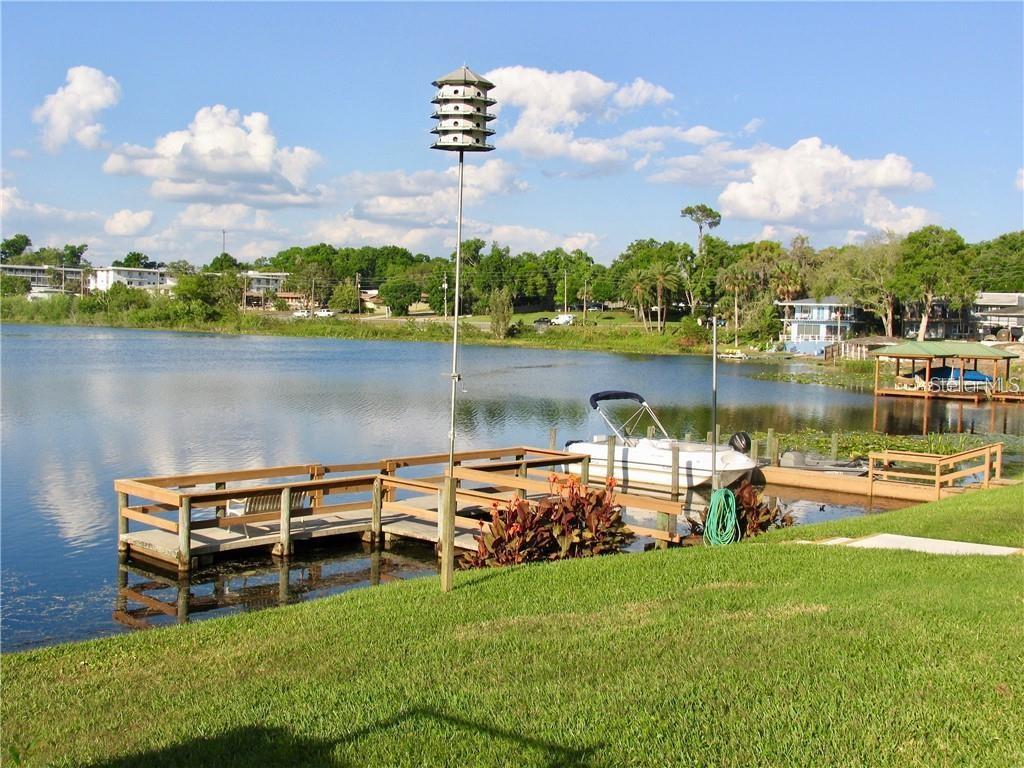 A wooden dock with a boat extends into a lake near a grassy lawn — 700 MIRROR TERRACE NW UNIT 506, WINTER HAVEN, FL