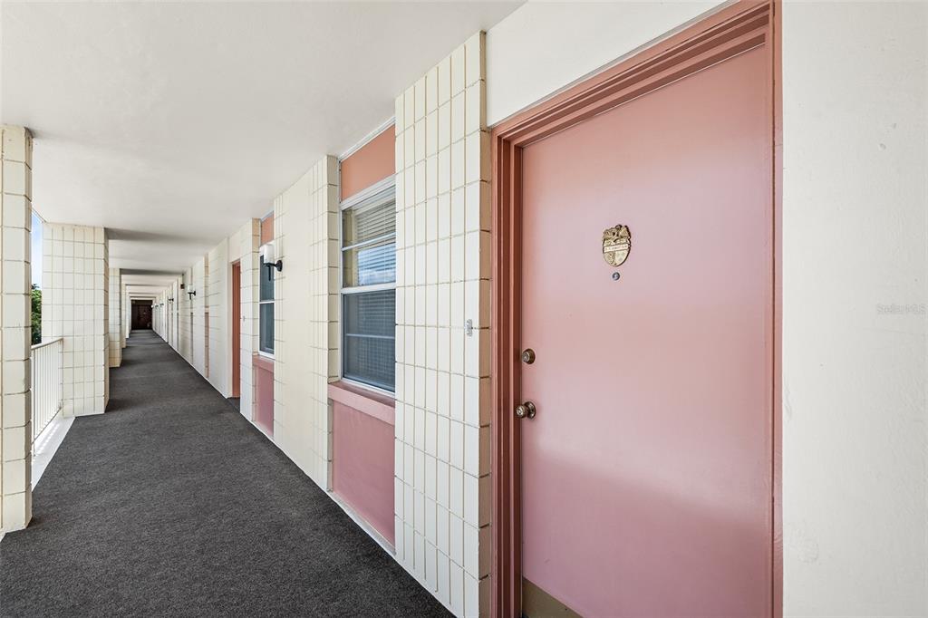 A long outdoor apartment corridor features pink doors, white tiled walls, and gray carpeting — 700 MIRROR TERRACE NW UNIT 506, WINTER HAVEN, FL
