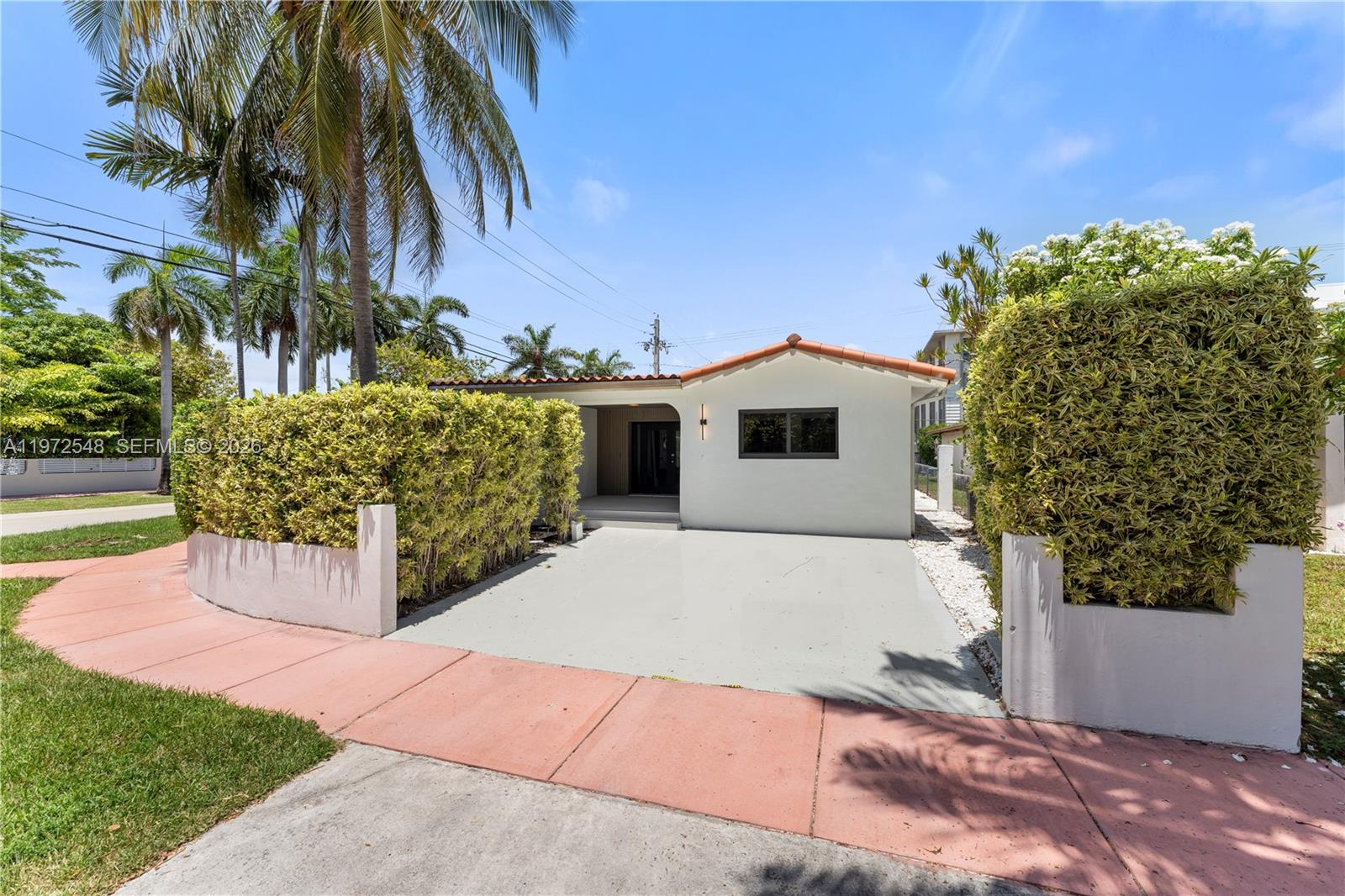 A single-story white house features a front driveway, a tiled roof, and tall privacy hedges — 1221 Biarritz Dr, Miami Beach FL 33141, MIAMI BEACH, FL