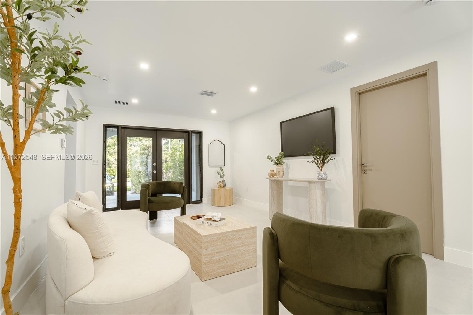 A modern living room features a curved white sofa, olive green chairs, and travertine furniture — 1221 Biarritz Dr, Miami Beach FL 33141, MIAMI BEACH, FL
