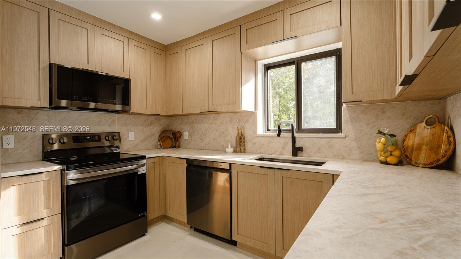 A kitchen features light wood cabinets, stainless steel appliances, and a marble-patterned countertop — 1221 Biarritz Dr, Miami Beach FL 33141, MIAMI BEACH, FL