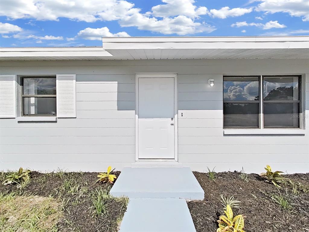 A light gray house exterior features a white front door, two windows, and landscaped mulch — 9667 BAYSIDE COURT, SPRING HILL, FL