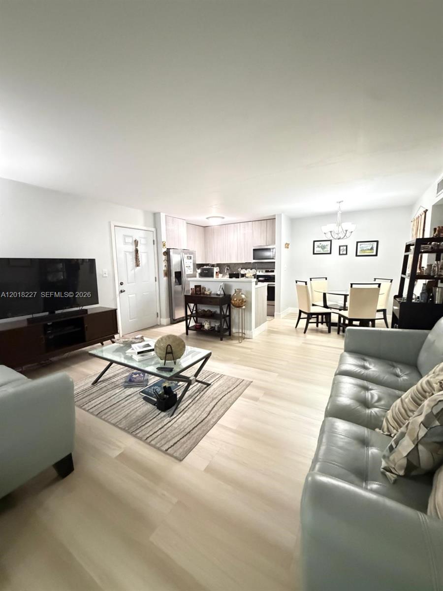This open-concept living and dining area features light wood-look flooring and a modern kitchen — 761 NE 199th St # 102, Miami FL 33179, MIAMI, FL