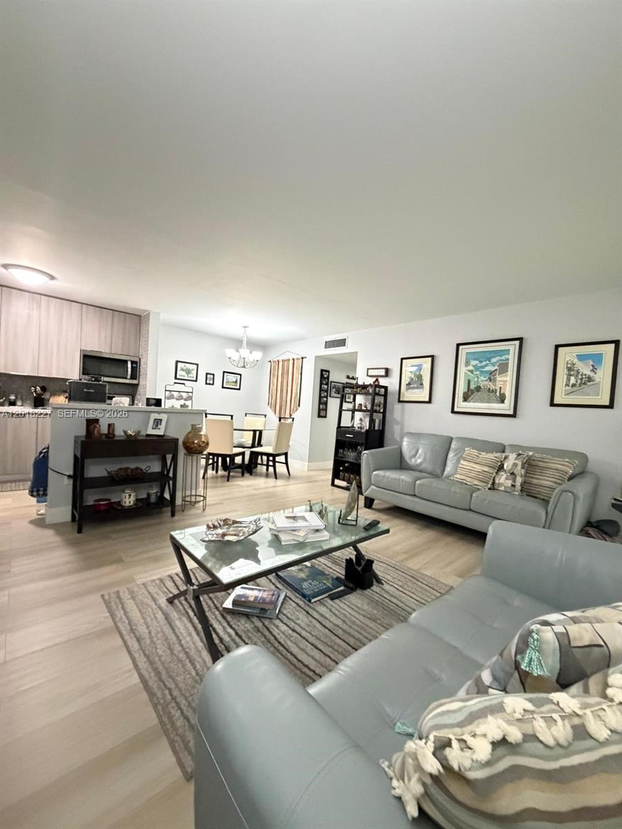 A living room with light-colored flooring, two gray sofas, and an open-concept kitchen — 761 NE 199th St # 102, Miami FL 33179, MIAMI, FL